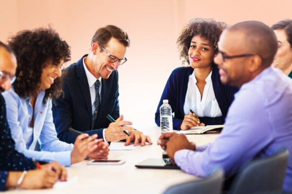 Groupe de managers en réunion, échange convivial et décontracté autour d’une table, avec notes et bouteille d’eau. communication non violente en management est présentée comme méthode.