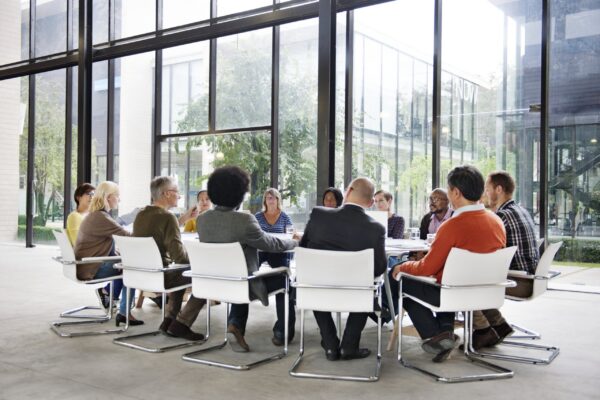 Groupe de personnes autour d’une table en réunion dans une salle lumineuse, discussions et échanges sur la différence entre conflit et désaccord.